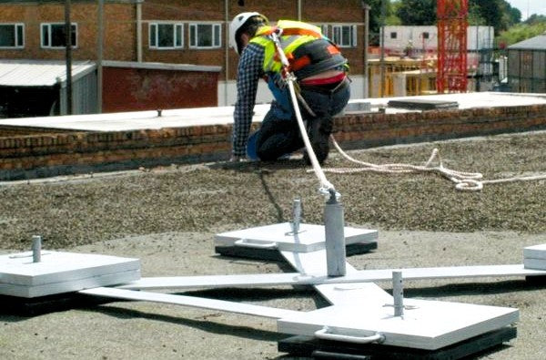 A worker uses a rooftop fall protection harness with anchor equipment.
