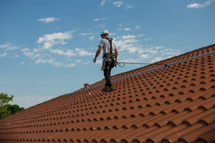 Man walking on a tile roof wearing a harness connected to a lifeline