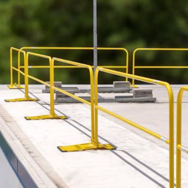 Yellow safety guardrail system with weighted bases installed on a flat roof.