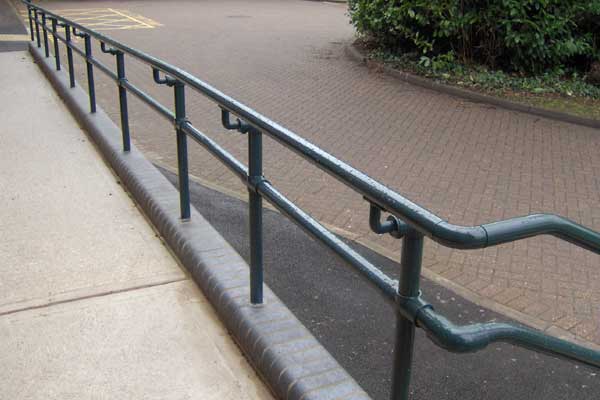 Metal ADA-compliant handrail and guardrail system installed along a paved outdoor walkway.
