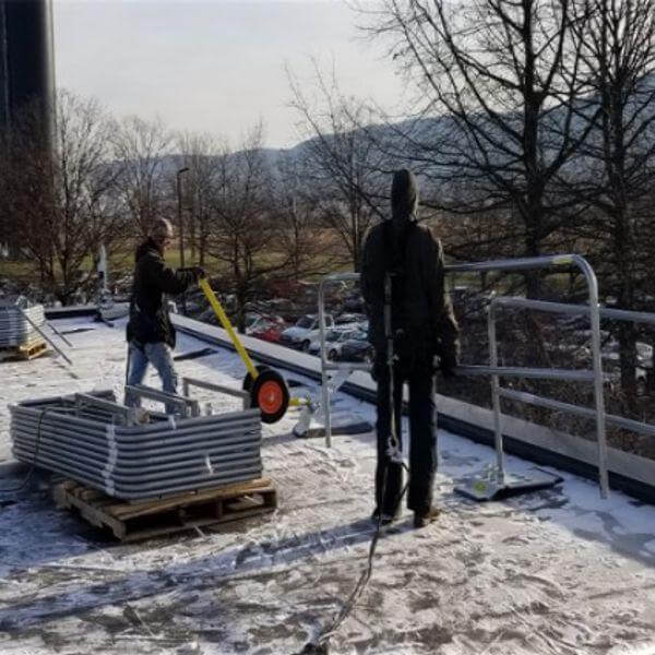 Two workers installing a non-penetrating rooftop safety rail system along the edge of a flat commercial roof.