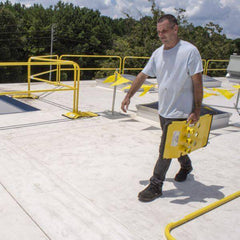 Worker carrying a yellow base for the Safety Rail Source NextGen 3000 Universal Guardrail System at a project site in Jacksonville, FL.