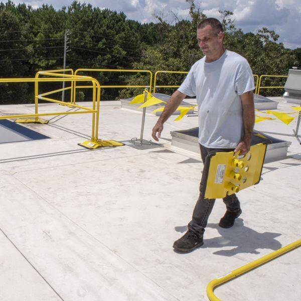 Worker carrying a yellow base for the Safety Rail Source NextGen 3000 Universal Guardrail System at a project site in Jacksonville, FL.