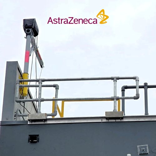 Industrial safety railing system with silver metal pipes and handrails mounted on a dark gray parapet, and an AstraZeneca logo on the front.