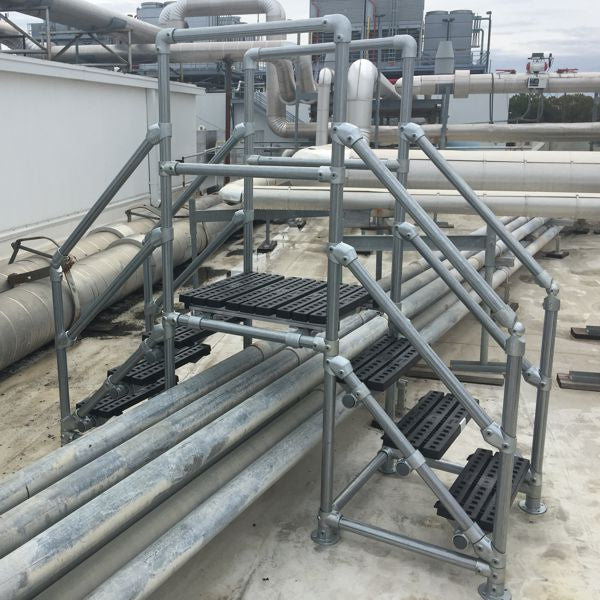 Metal crossover rooftop stairs installed on a commercial roof to safely navigate over pipes and ductwork.