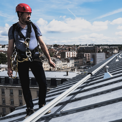 Man in hardhat wearing a harness walking across a roof