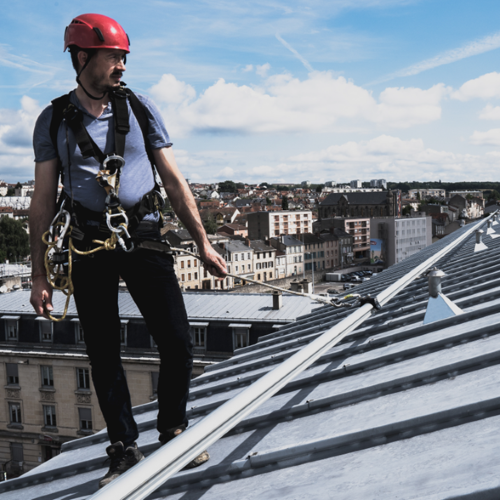 Man in hardhat wearing a harness walking across a roof