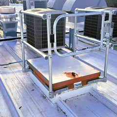 Galvanized steel safety guardrail installed around a roof hatch on a commercial metal roof.