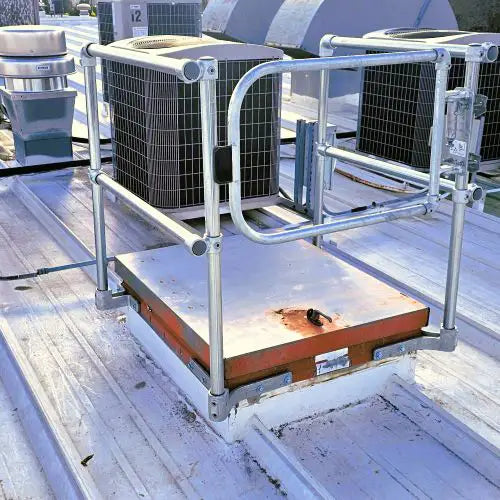 Galvanized steel safety guardrail installed around a roof hatch on a commercial metal roof.