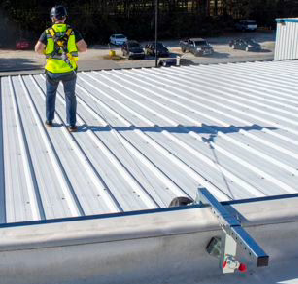 Worker walking across a roof wearing a harness connected to a roof achor