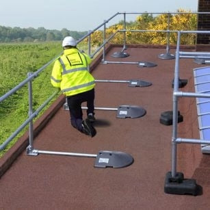 Technician wearing safety gear inspecting a rooftop fitted with a freestanding KeeGuard modular guardrail system.