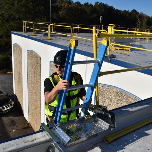 Man in hardhat climbing an extension ladder onto the roof.