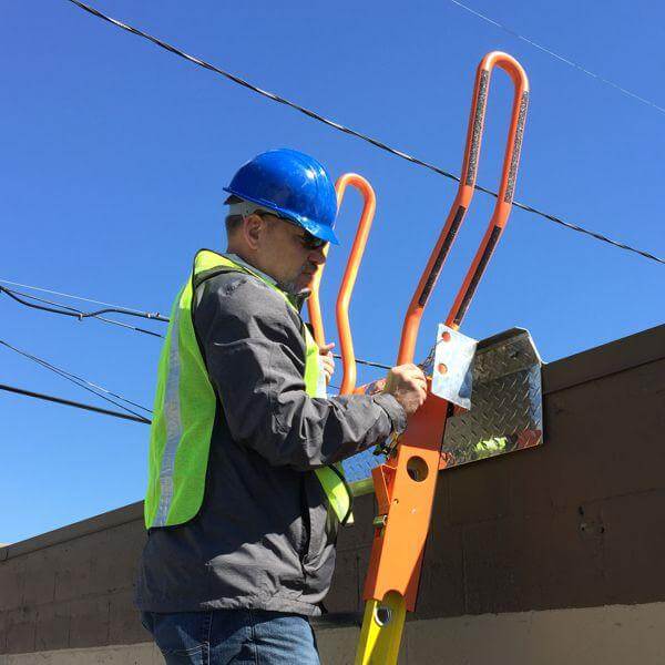 Worker attaching Safety Rail Source WalkThru extension ladder safety extension handles to prevent ladder fall accidents.