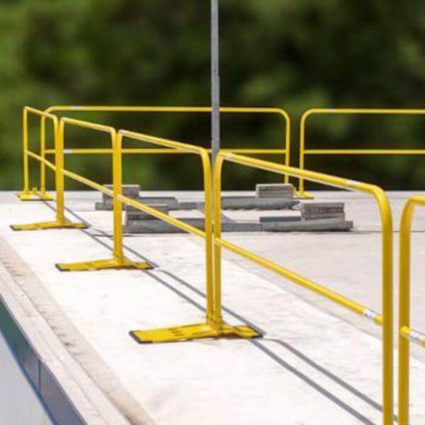 Yellow safety guardrail system with weighted bases installed on a flat surface or roof.