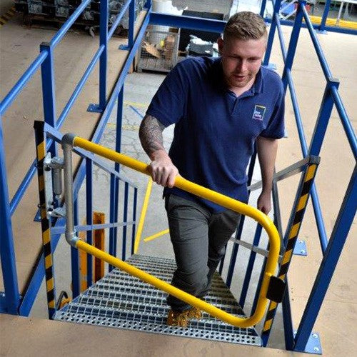Man climbing a metal stair case with a yellow safety gate at the top.