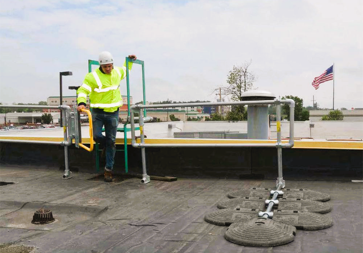 Man in hardhat and safety vest climbing onto a flat roof from a ladder.