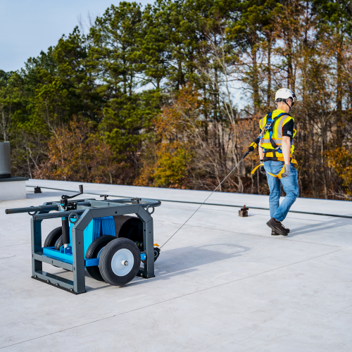 Man on a rooftop wearing a harness connected to a mobile fall protection anchor