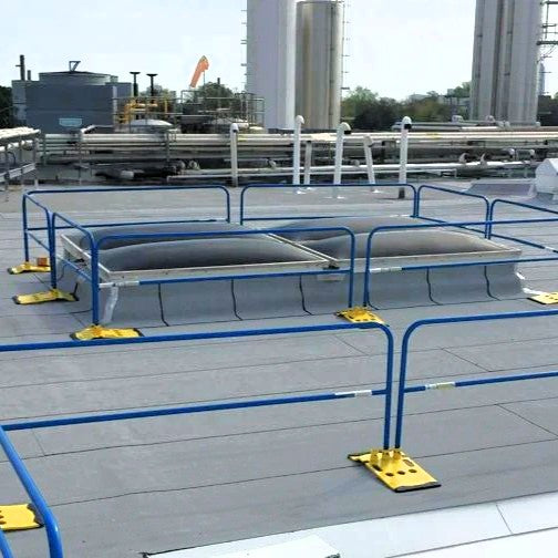 Commercial rootop with skylights protected by blue railing with yellow bases.