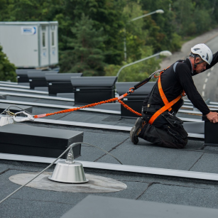 Worker wearing a safety harness and hard hat working on a flat roof connected to a personal fall arrest system.