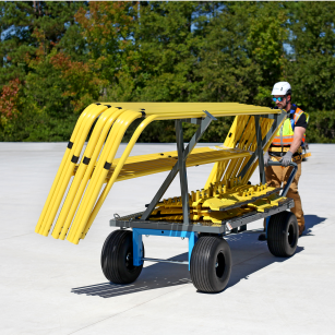 Worker transporting a mobile safety rail cart loaded with yellow guardrails across a flat roof.