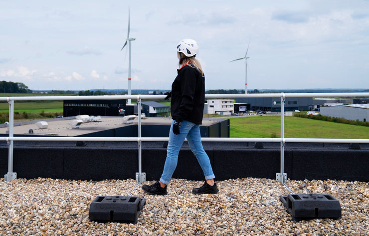 Worker walking along a rooftop equipped with Safety Rail Source non-penetrating aluminum railing systems for commercial fall protection.