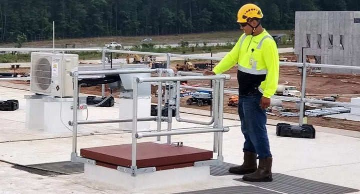 A worker on the roof next to a hatch surrounded by safety railing.
