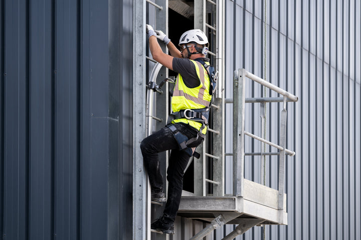Worker wearing safety harness and gear climbing a fixed ladder using a vertical lifeline system.