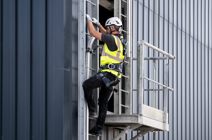 Worker wearing safety harness and gear climbing a fixed ladder using a vertical lifeline system.