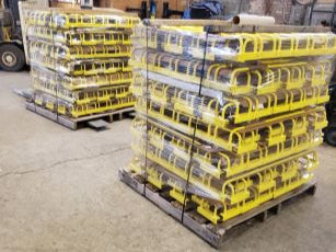 Stacked pallets of yellow safety guardrails wrapped and ready for shipment in a warehouse.