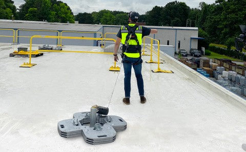 A worker uses a rooftop fall protection anchor near portable guardrails.