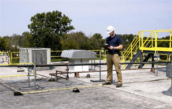 Person on a rooftop inspecting equipment with a tablet