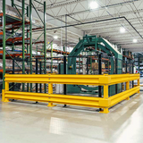 A large industrial safety guardrail system with bright yellow tubular rails and a green metal frame, installed in a warehouse setting.