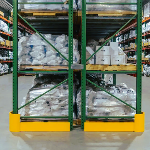 Green industrial warehouse shelving with yellow base protectors, holding pallets stacked with white packaged goods in a warehouse aisle.