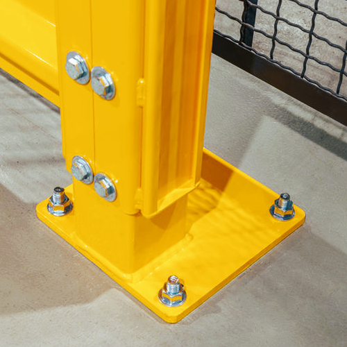 A close-up of a bright yellow metal support post anchored to a square base plate with multiple silver bolts and nuts, set on a concrete floor.