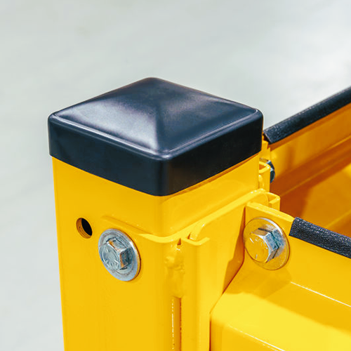 Close-up of a bright yellow metal safety barrier or guardrail post with a black protective cap and silver bolts.