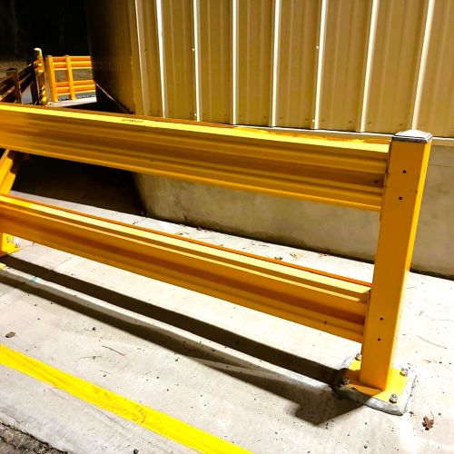 Yellow safety barrier on a concrete floor with a corrugated metal wall in the background.