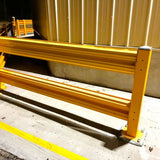 Yellow safety barrier on a concrete floor with a corrugated metal wall in the background.