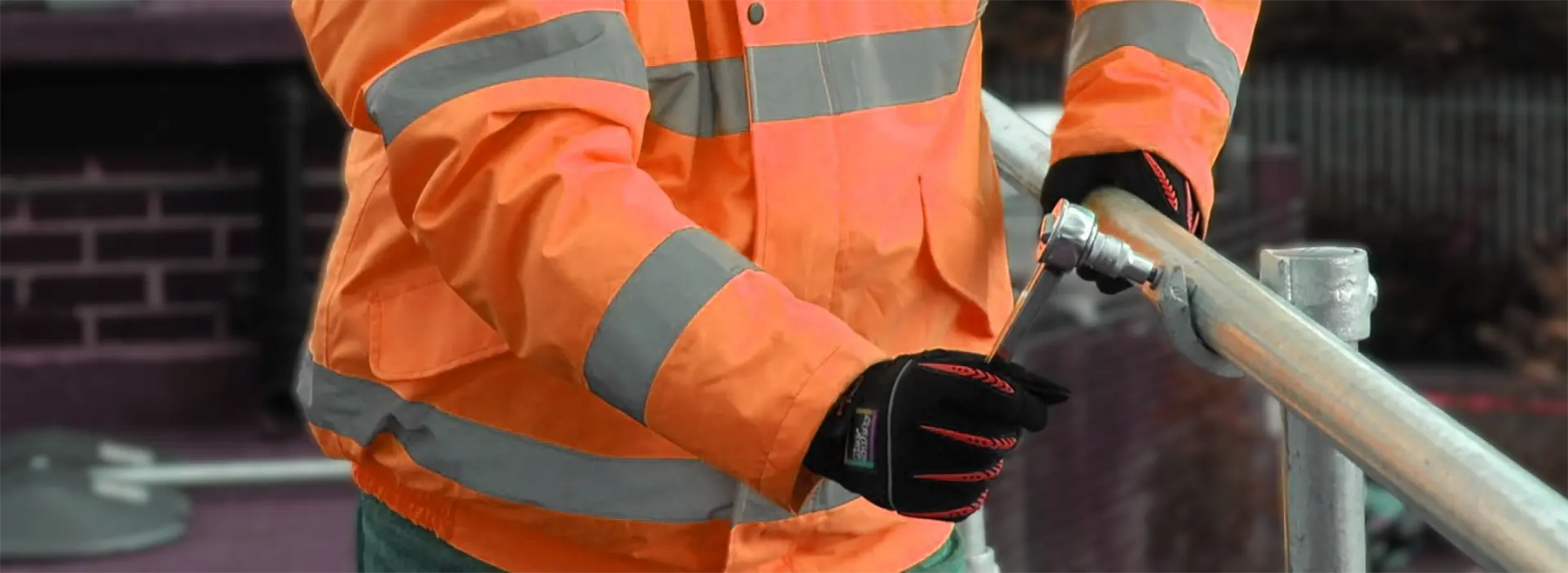 Person wearing an orange high-visibility jacket holding a tool
