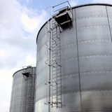 NextGen Mighty-Lite Fixed Ladder - Two large metal silos with ladders against a blue sky.