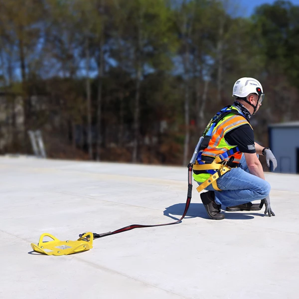 Person on a roof wearing safety gear with a yellow safety device on a clear day.