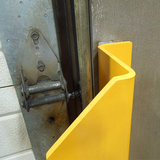 A bright yellow plastic door stopper mounted on a metal door frame next to a gray wall.